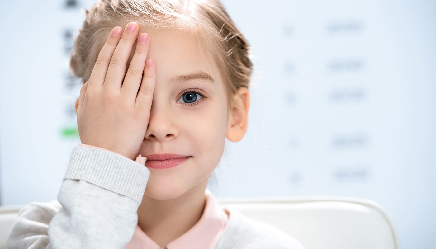a young girl covering her right eye with her hand