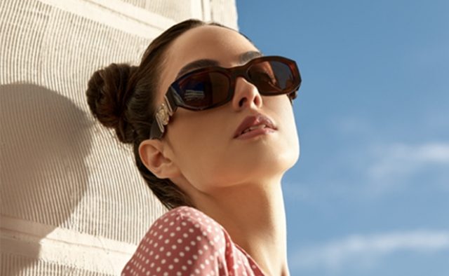Woman leaning against a wall with the sky in the background wearing sunglasses and pink polkadot shirt