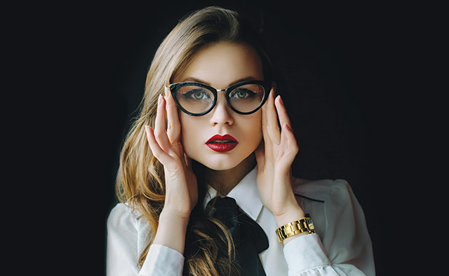 Photo: black background with woman wearing a black and white blouse, red lipstick and eyeglasses
