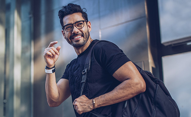 Photo: Smiling man wearing eyeglases and a black t-shirt with a backpack over his shoulder
