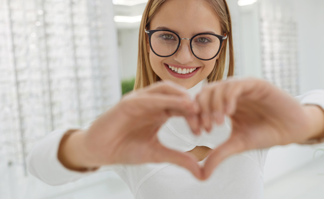 Woman wearing glasses with her hands making a heart shape