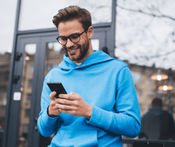 Man wearing glasses, outdoors and looking down at his cellphone