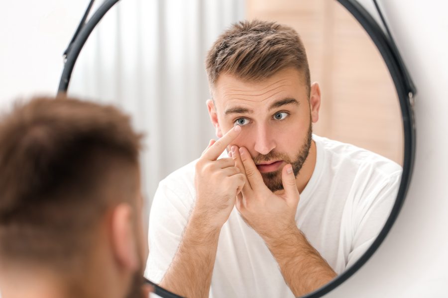 Man looking in the mirror as he puts in his contact lenses